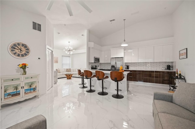 kitchen with appliances with stainless steel finishes, a kitchen breakfast bar, tasteful backsplash, pendant lighting, and white cabinetry