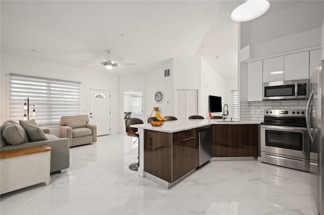 kitchen with kitchen peninsula, decorative backsplash, appliances with stainless steel finishes, dark brown cabinets, and white cabinetry