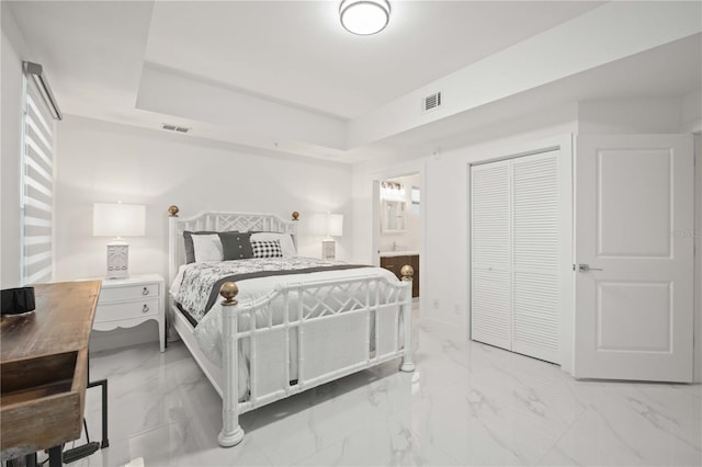 bedroom featuring ensuite bathroom, a tray ceiling, and a closet