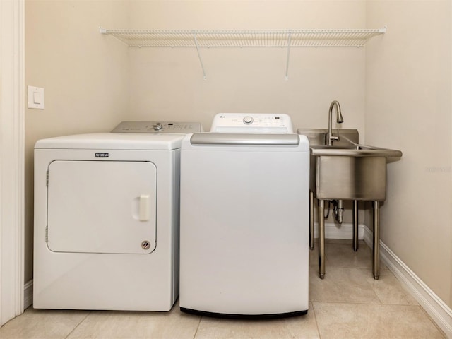 laundry area featuring light tile patterned floors, washer and clothes dryer, and sink