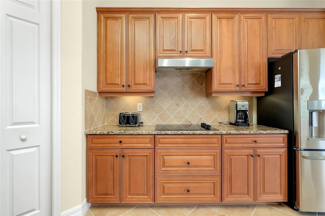 kitchen featuring light stone countertops, tasteful backsplash, stainless steel refrigerator with ice dispenser, black electric cooktop, and light tile patterned floors