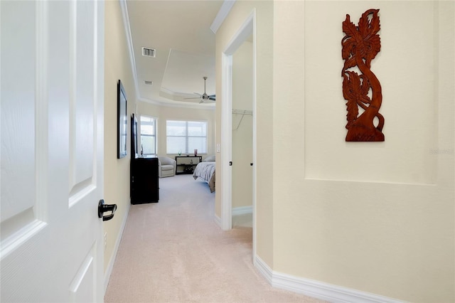 hallway featuring a raised ceiling, light colored carpet, and ornamental molding