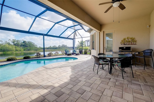 view of pool with area for grilling, ceiling fan, a water view, glass enclosure, and a patio