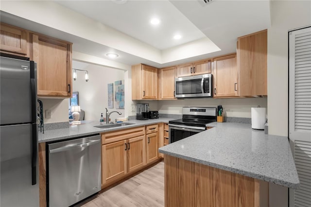 kitchen with kitchen peninsula, light stone countertops, stainless steel appliances, light brown cabinets, and light hardwood / wood-style floors