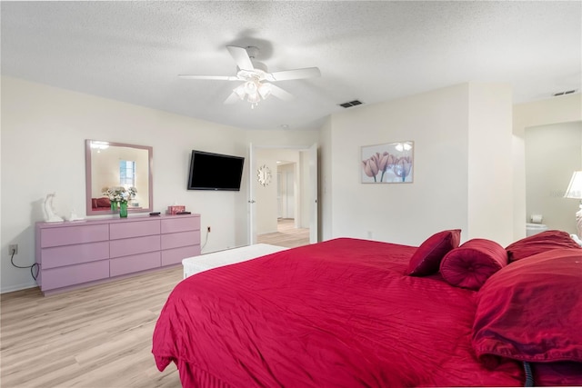 bedroom featuring a textured ceiling, light wood-type flooring, ensuite bathroom, and ceiling fan