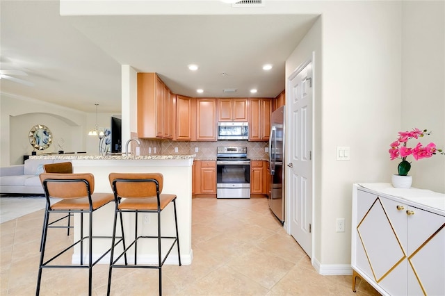 kitchen featuring backsplash, ceiling fan with notable chandelier, appliances with stainless steel finishes, a kitchen bar, and kitchen peninsula