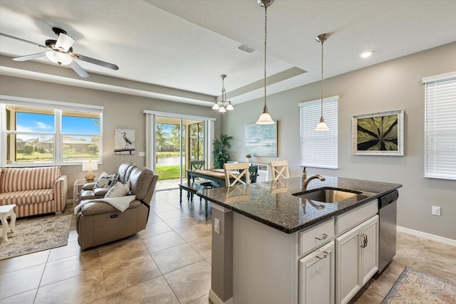 kitchen featuring dishwasher, dark stone counters, an island with sink, sink, and a raised ceiling