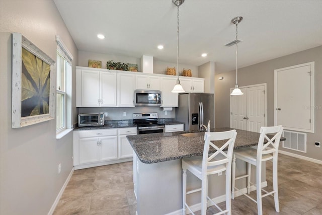 kitchen with white cabinets, pendant lighting, appliances with stainless steel finishes, and an island with sink