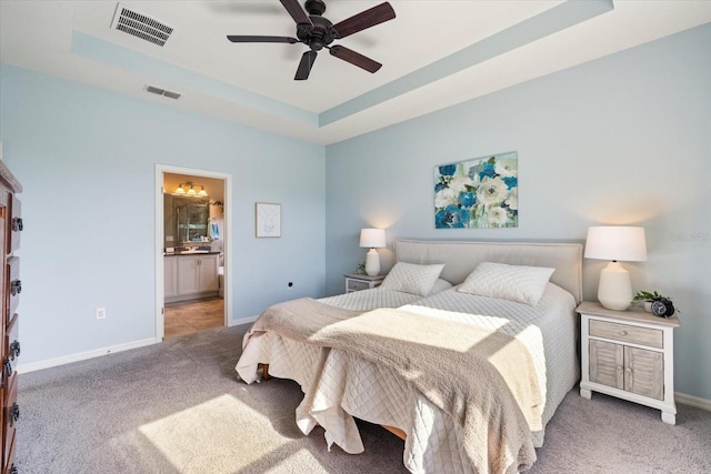 carpeted bedroom featuring ensuite bathroom, ceiling fan, and a tray ceiling