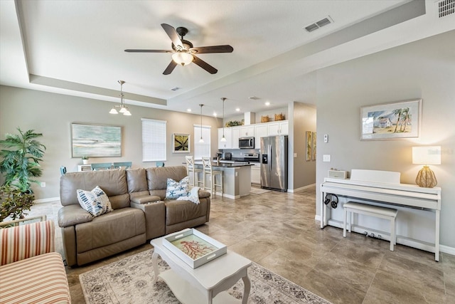 living room with ceiling fan with notable chandelier and a tray ceiling