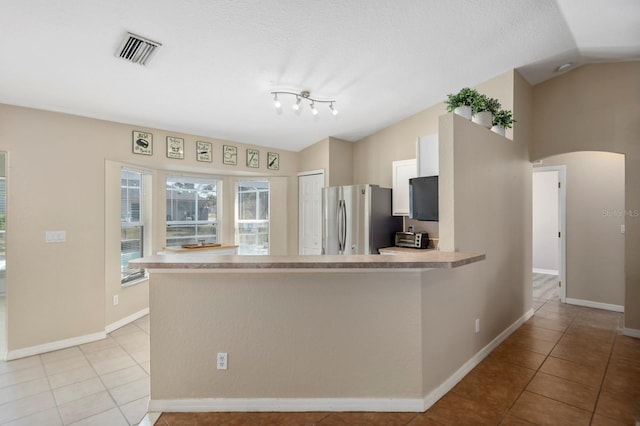 kitchen featuring stainless steel fridge, light tile patterned floors, kitchen peninsula, and vaulted ceiling