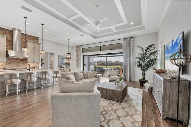 living room with a raised ceiling, ceiling fan, ornamental molding, and light wood-type flooring