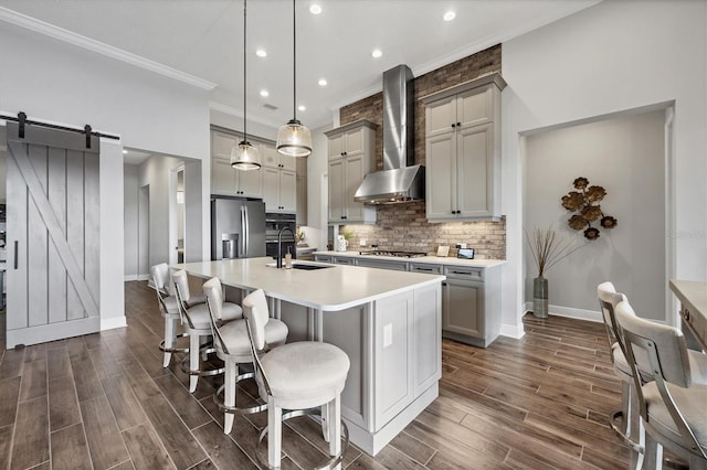 kitchen featuring wall chimney exhaust hood, hanging light fixtures, a barn door, dark hardwood / wood-style flooring, and appliances with stainless steel finishes