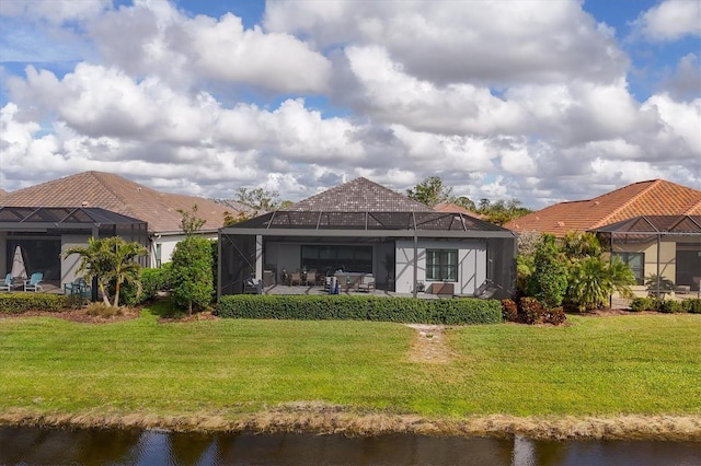 rear view of house with a lanai, a lawn, and a water view