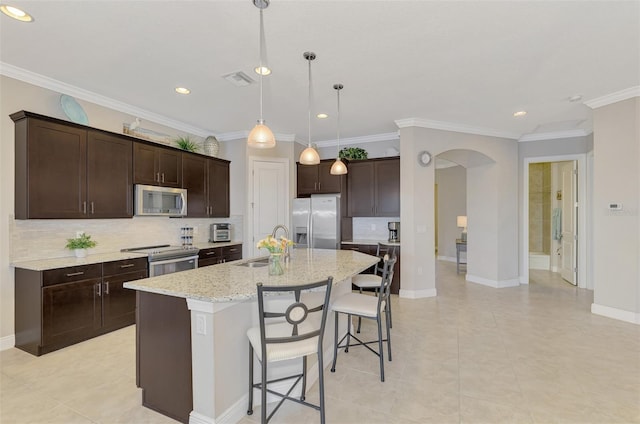 kitchen featuring a center island with sink, hanging light fixtures, ornamental molding, appliances with stainless steel finishes, and a kitchen bar