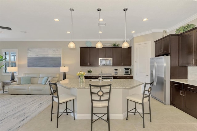 kitchen featuring light stone countertops, an island with sink, appliances with stainless steel finishes, decorative light fixtures, and a kitchen bar