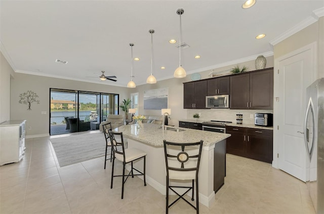 kitchen with pendant lighting, a center island with sink, ceiling fan, ornamental molding, and appliances with stainless steel finishes