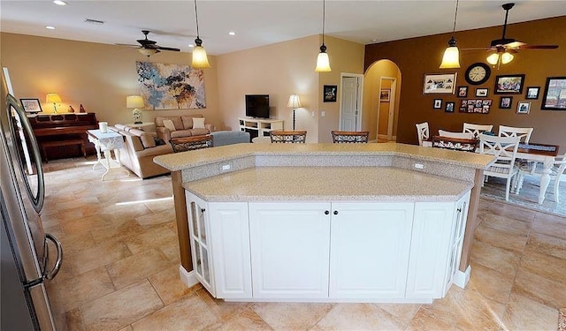 kitchen featuring white cabinets, decorative light fixtures, stainless steel refrigerator, and a kitchen island