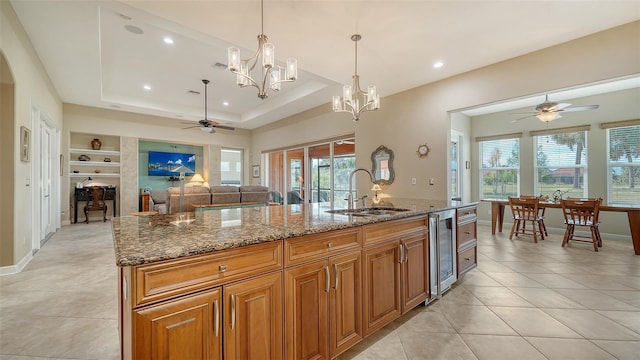 kitchen with a kitchen island with sink, beverage cooler, sink, stone counters, and hanging light fixtures