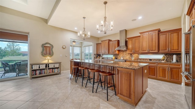 kitchen with tasteful backsplash, wall chimney exhaust hood, a kitchen island with sink, pendant lighting, and dark stone countertops