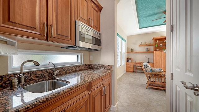 kitchen featuring lofted ceiling, dark stone countertops, light tile patterned floors, and sink