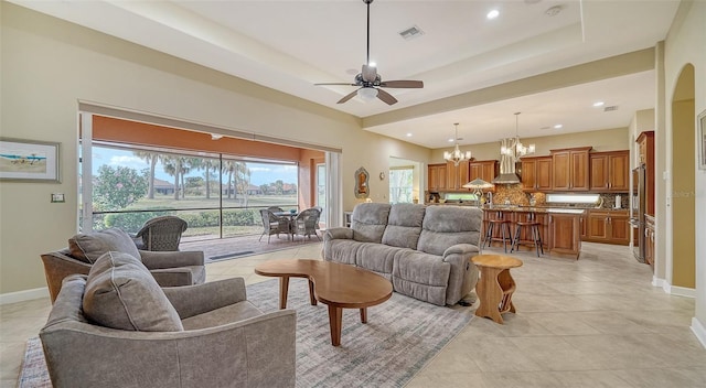 tiled living room with ceiling fan with notable chandelier and a raised ceiling