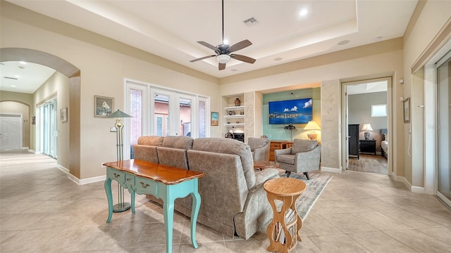 living room with ceiling fan, a raised ceiling, light tile patterned floors, and built in shelves