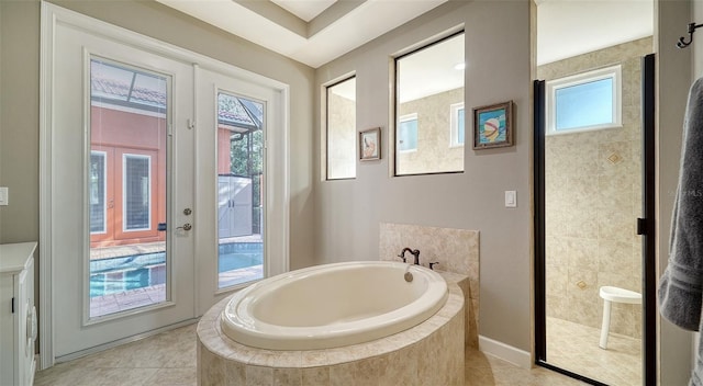 bathroom featuring french doors, a relaxing tiled tub, tile patterned floors, and plenty of natural light