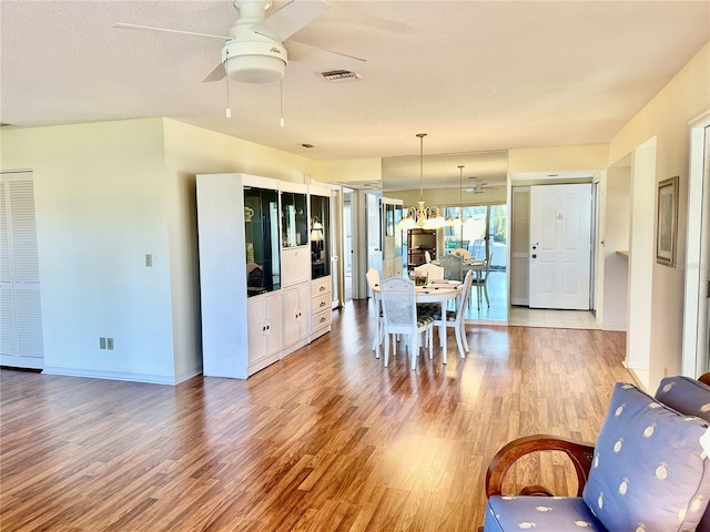 dining space with ceiling fan with notable chandelier, a textured ceiling, and light wood-type flooring