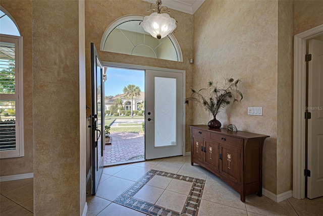 entryway with a high ceiling, crown molding, light tile patterned floors, and a wealth of natural light