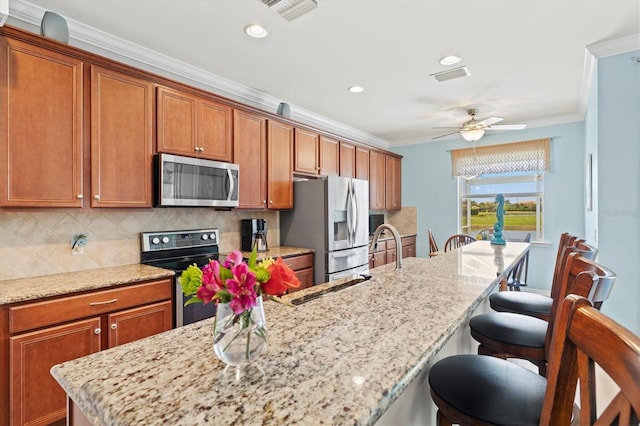 kitchen with light stone counters, a breakfast bar area, decorative backsplash, appliances with stainless steel finishes, and ornamental molding