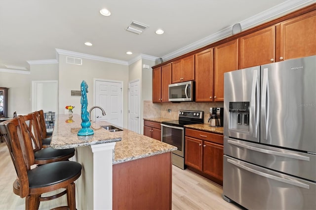 kitchen with light stone countertops, appliances with stainless steel finishes, light wood-type flooring, sink, and a center island with sink