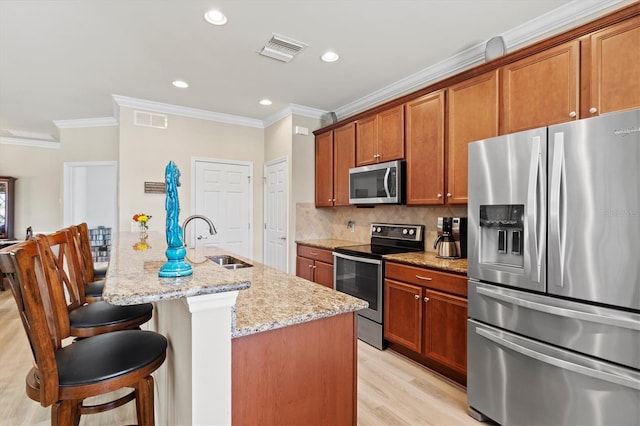 kitchen featuring light stone countertops, sink, stainless steel appliances, light hardwood / wood-style floors, and a center island with sink