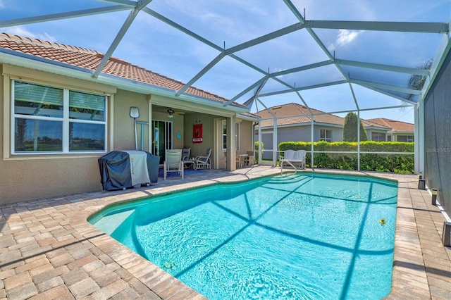 view of swimming pool featuring glass enclosure, ceiling fan, a patio, and grilling area