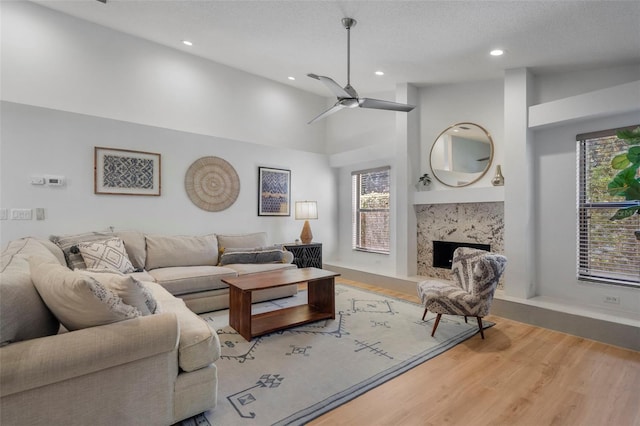 living room with a textured ceiling, ceiling fan, hardwood / wood-style flooring, high vaulted ceiling, and a fireplace