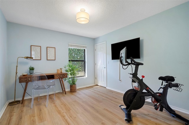 exercise area featuring light wood-type flooring and a textured ceiling