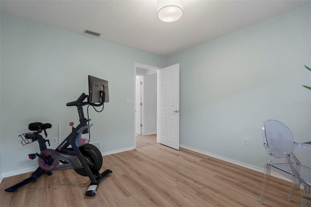 workout room with a textured ceiling and light wood-type flooring