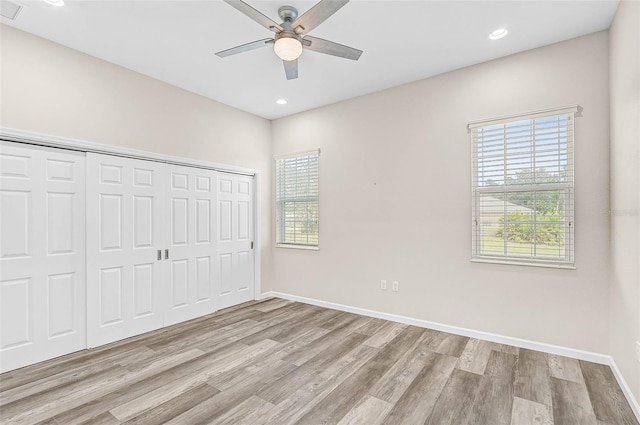 unfurnished bedroom with ceiling fan, a closet, light hardwood / wood-style flooring, and multiple windows