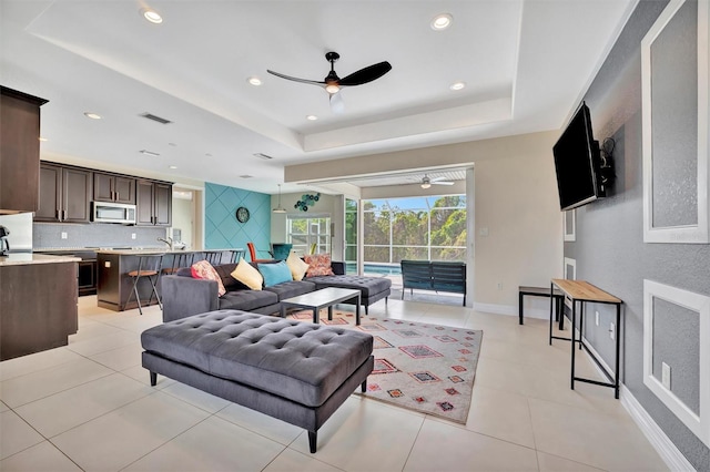 living room featuring ceiling fan, a raised ceiling, and light tile patterned floors