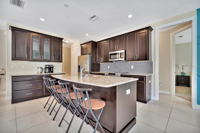 kitchen featuring a breakfast bar, a kitchen island with sink, dark brown cabinets, and stainless steel appliances