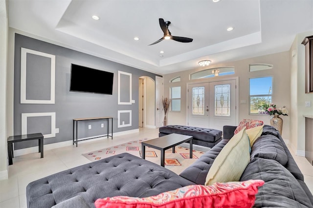 tiled living room with ceiling fan, a raised ceiling, and french doors