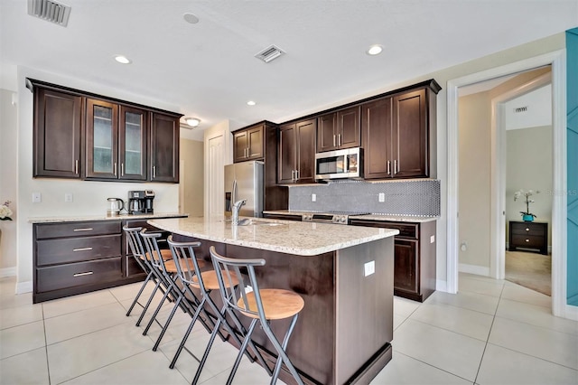 kitchen with a breakfast bar, dark brown cabinets, stainless steel appliances, and a kitchen island with sink