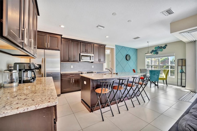 kitchen with pendant lighting, a kitchen island with sink, sink, light stone counters, and stainless steel appliances