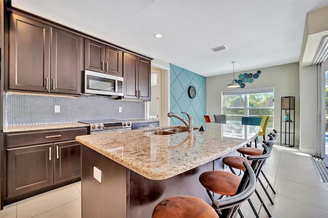 kitchen with a breakfast bar, a kitchen island with sink, sink, appliances with stainless steel finishes, and dark brown cabinets