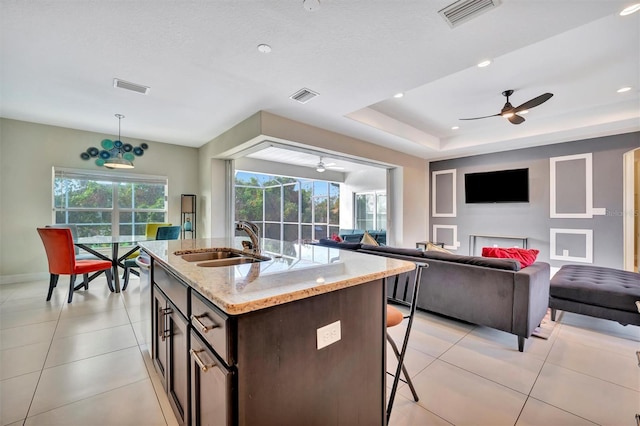 kitchen with light stone countertops, dark brown cabinetry, a kitchen island with sink, sink, and pendant lighting