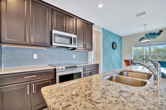 kitchen featuring pendant lighting, sink, light stone counters, dark brown cabinetry, and stainless steel appliances