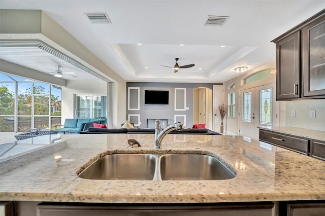 kitchen with a raised ceiling, light stone counters, dark brown cabinets, and sink