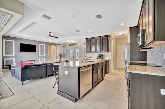 kitchen with ceiling fan, sink, a raised ceiling, an island with sink, and appliances with stainless steel finishes