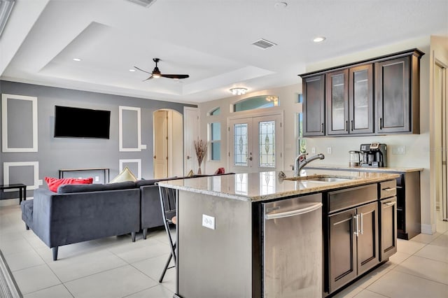 kitchen featuring a raised ceiling, sink, an island with sink, and dark brown cabinets