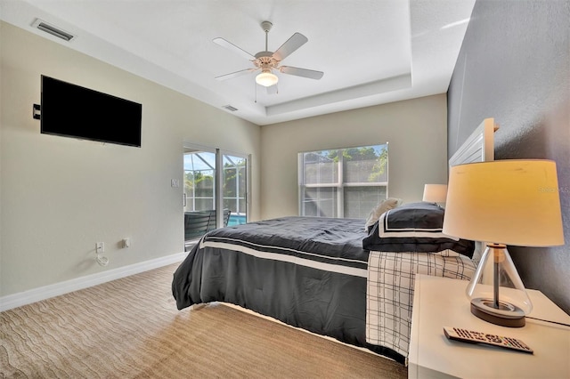 carpeted bedroom featuring a tray ceiling, multiple windows, ceiling fan, and access to outside